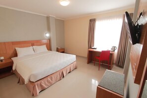 A hotel room with a large bed, a desk with a chair, a television, and a window with curtains.