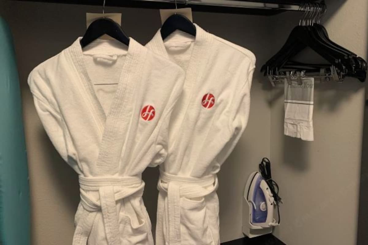 Two white robes with red logos hanging on a rack.