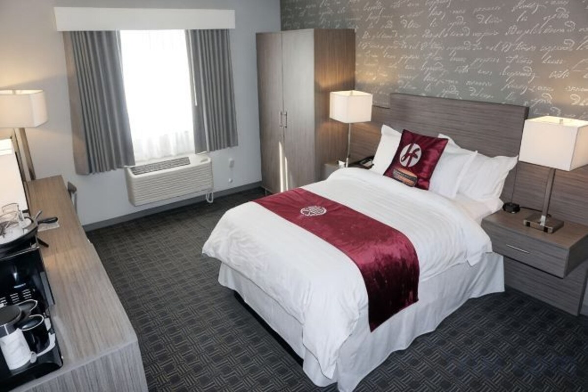 A hotel room with a large bed, bedside tables, a desk, and a window with curtains.