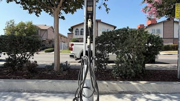 Una estación de carga pública para vehículos eléctricos en una zona residencial con casas al fondo.