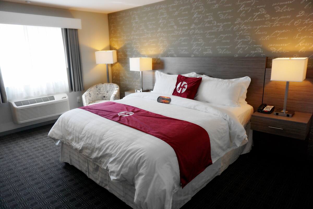 A hotel room with a large bed, two bedside lamps, a chair, and a wall with decorative writing.