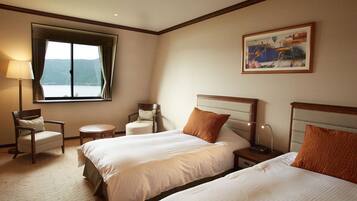 A hotel room with two beds, a chair, a small table, a lamp, and a painting on the wall.