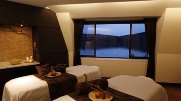 Ein Hotelzimmer mit zwei Betten, einem kleinen Tisch mit Kerzen und Blick auf einen See im Abenddämmerung.