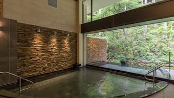 A spa area with a stone wall, a glass window, and a view of greenery outside.