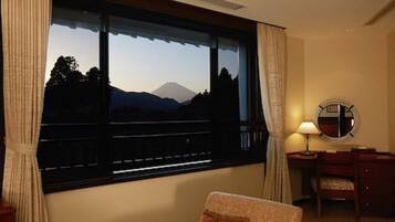 A hotel room with a large window offering a mountain view, a desk with a lamp, and a chair.