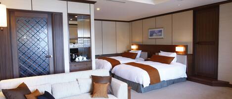A hotel room with two beds, a sofa, a coffee table, and a minibar.