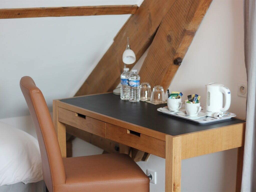 Una pequeña mesa de madera con tapa negra, una silla de cuero marrón y un hervidor blanco.