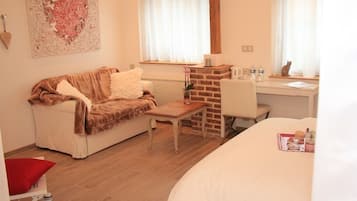 Una habitación acogedora con sofá, una mesita, chimenea de ladrillo y ventana con cortinas.