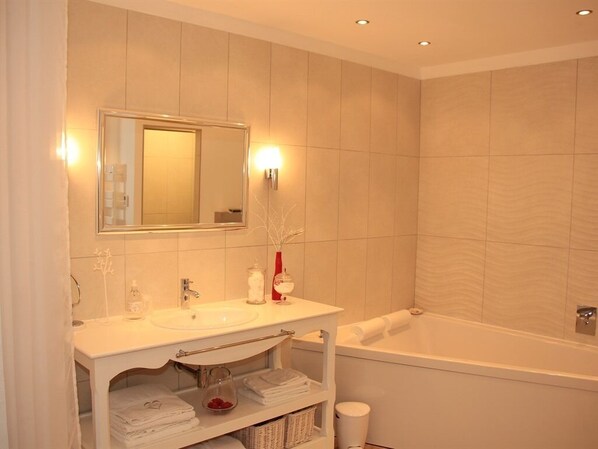 A modern bathroom with a white vanity, a large mirror, a bathtub, and a towel rack. - Au Coeur Des Hôtes (Steenvoorde)