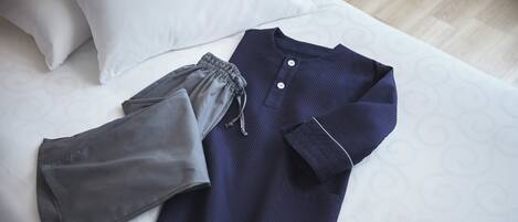 Una cama bien tendida con una almohada blanca y una prenda azul y gris sobre ella.