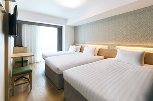 Habitación de hotel con dos camas, un escritorio, una silla y un televisor.