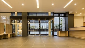 Un vestíbulo amplio con diseño moderno, que cuenta con un gran acceso de vidrio, un mostrador de recepción y una zona de estar con paneles de madera.
