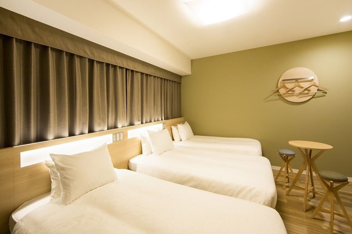 A hotel room with two beds, a small table, and a wall-mounted light fixture.