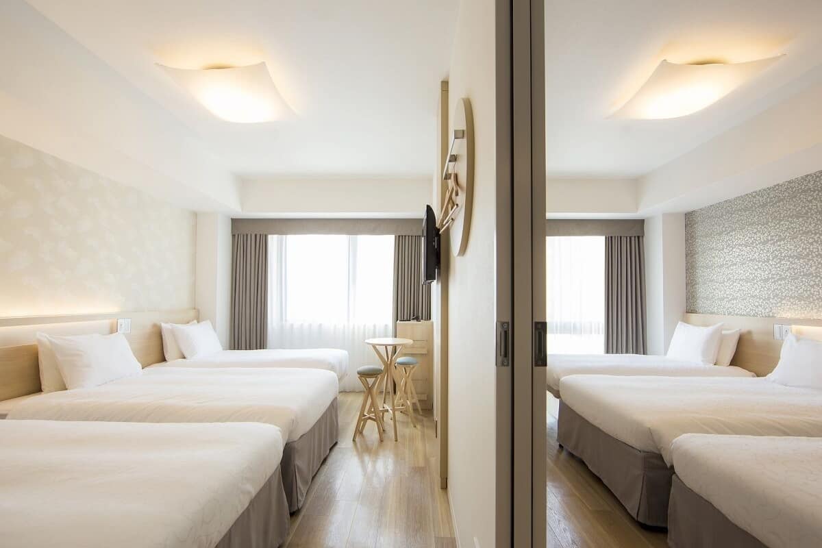 Hotellihuone, jossa on kolme sänkyä, pieni pöytä ja televisio.