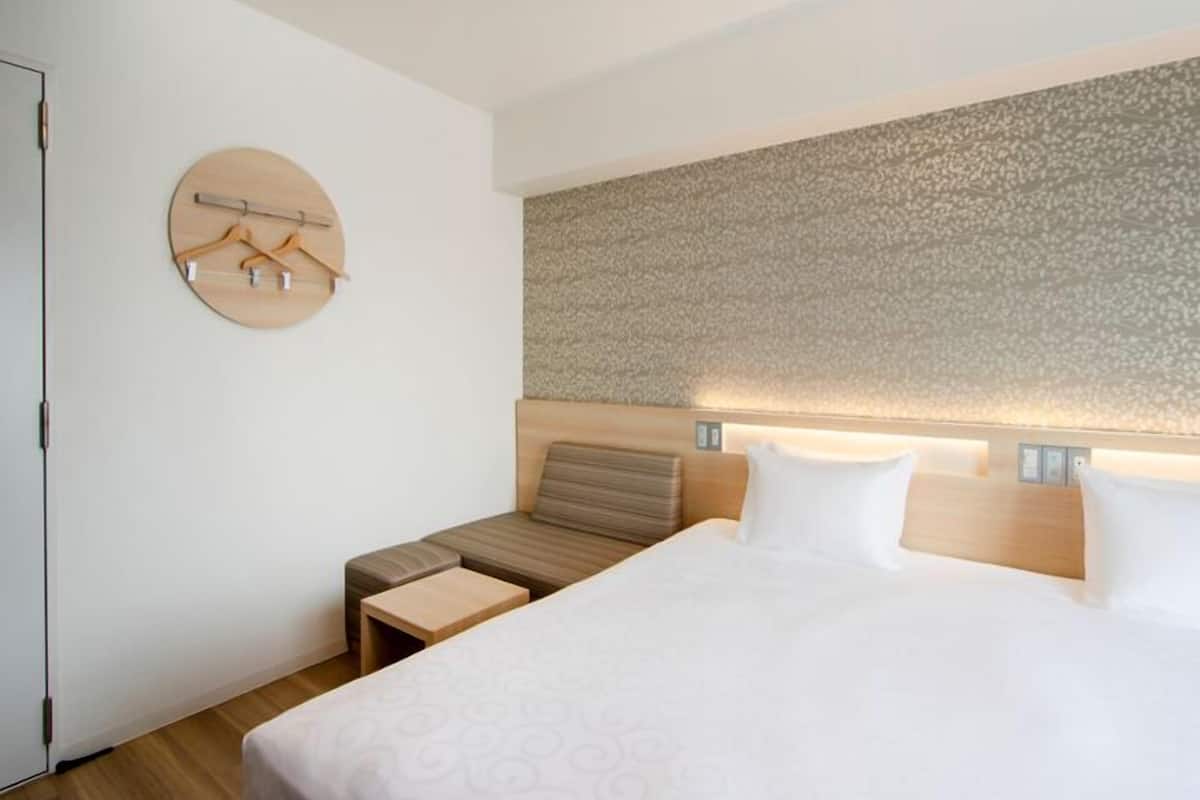 A hotel room with a bed, bedside tables, a round wall-mounted coat rack, and a textured wall.