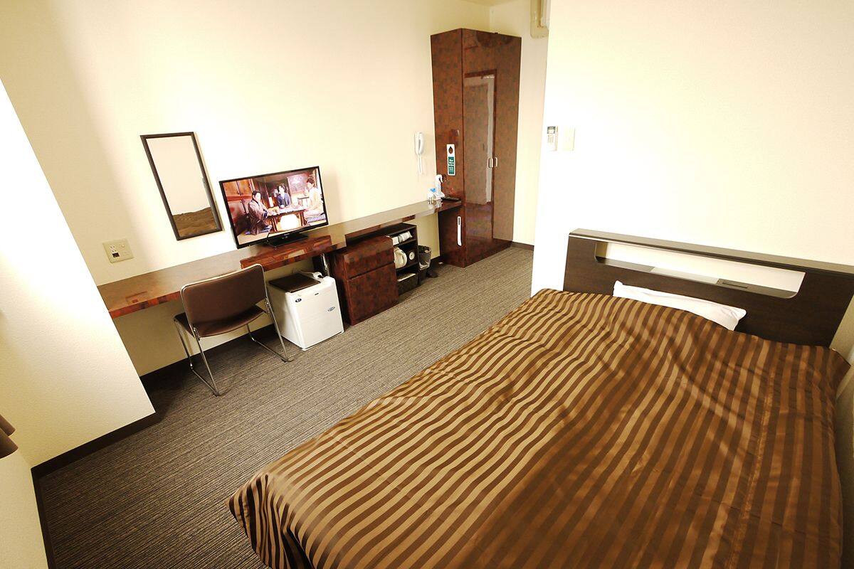 Une chambre d’hôtel équipée d’un lit, d’un bureau, d’une chaise, d’une télévision et d’une armoire.