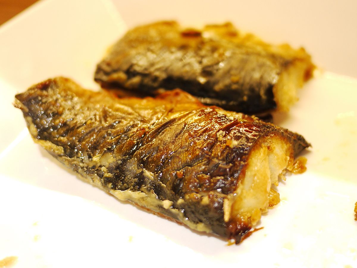 A close-up of a cooked fish with a crispy skin, served on a white plate.
