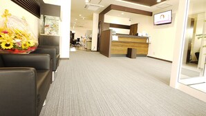 A reception area with a reception desk, a waiting area with chairs, and a television mounted on the wall. - Business Hotel Fiz Nagoya Airport (Toyoyama)