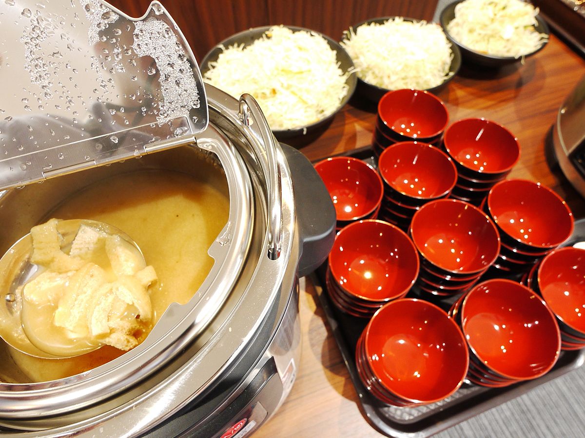A buffet setup with a soup station and bowls of shredded potatoes.