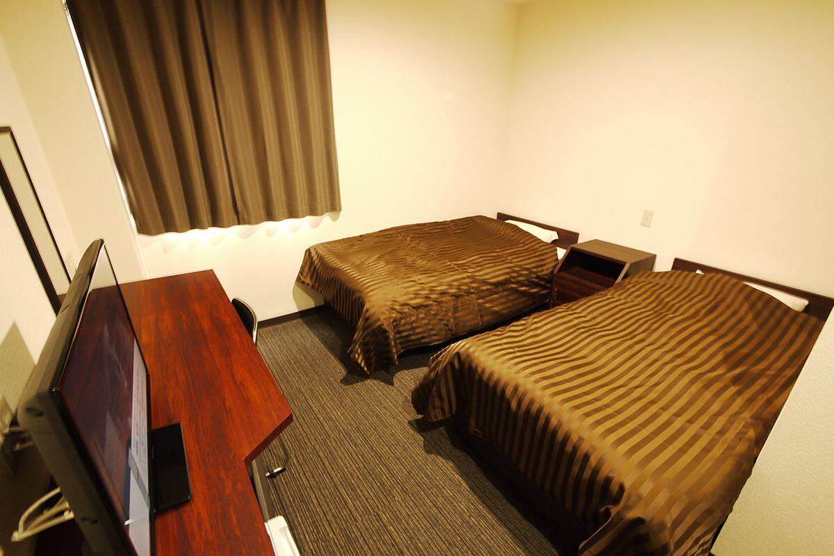 Une chambre d’hôtel avec deux lits simples, un bureau avec un ordinateur et une fenêtre avec des rideaux.