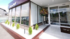 A modern building with large windows, a flower arrangement outside, and a clear sky. - Business Hotel Fiz Nagoya Airport (Toyoyama)