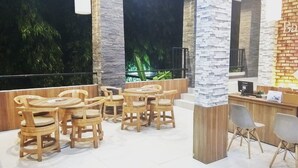 A cozy outdoor seating area with wooden tables and chairs, a reception desk, and a view of greenery. - Bali De Anyer Hotel and Restaurant (Carita)