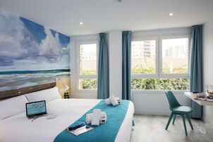 Une chambre d’hôtel avec un lit, un bureau, une chaise, un ordinateur portable et un tableau représentant une scène de plage.