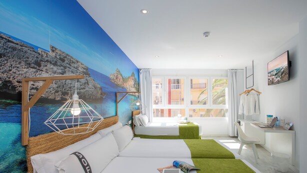 Une chambre d’hôtel moderne, dotée d’un grand lit, d’un bureau et offrant une vue sur la mer par la fenêtre.