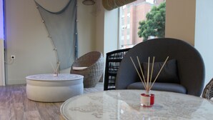 Un salon moderne avec une table ronde en verre, un canapé gris et un fauteuil en osier.