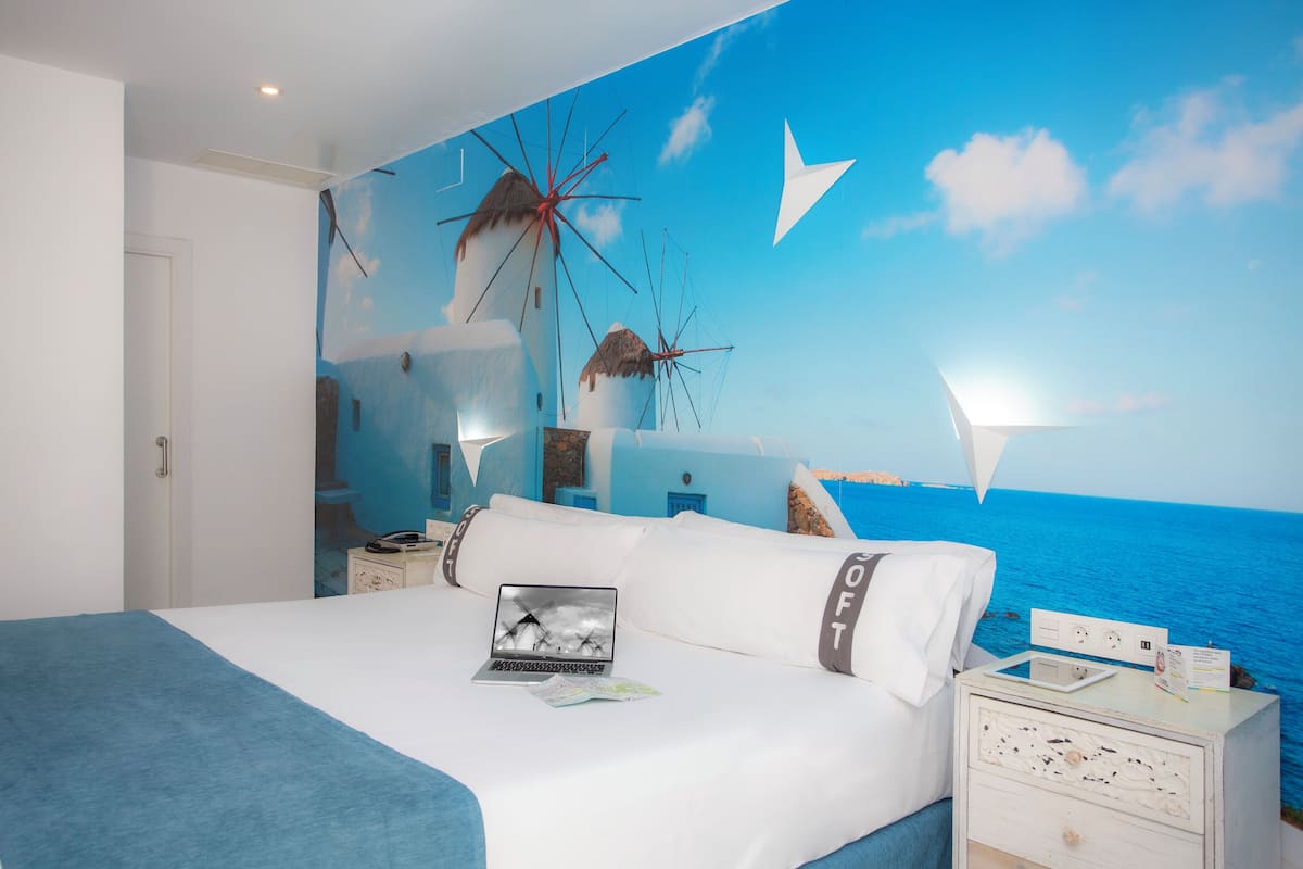 Een slaapkamer met een muurschildering van windmolens, een laptop en een nachtkastje met een lamp.