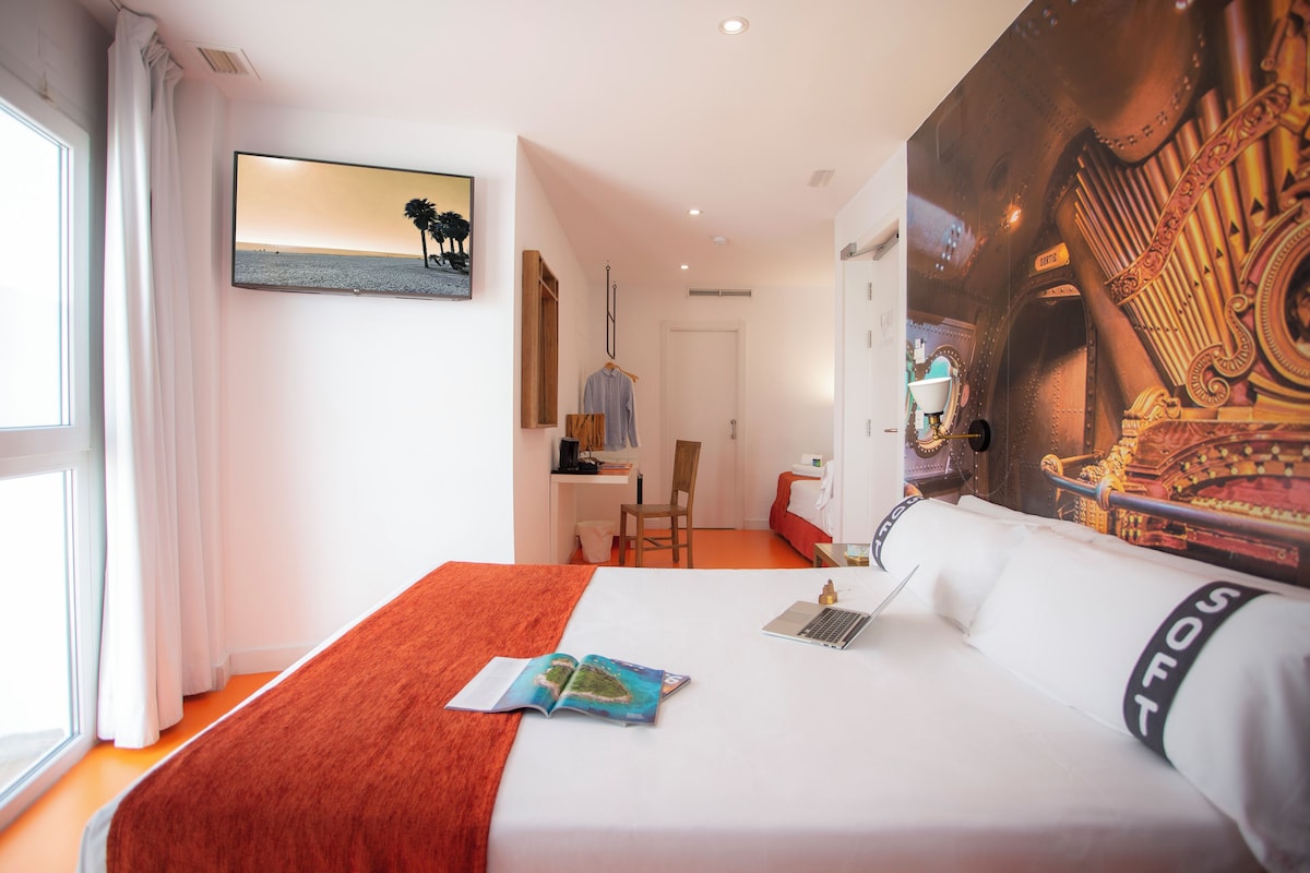 Een hotelkamer met een bed, een bureau, een stoel en een groot raam.