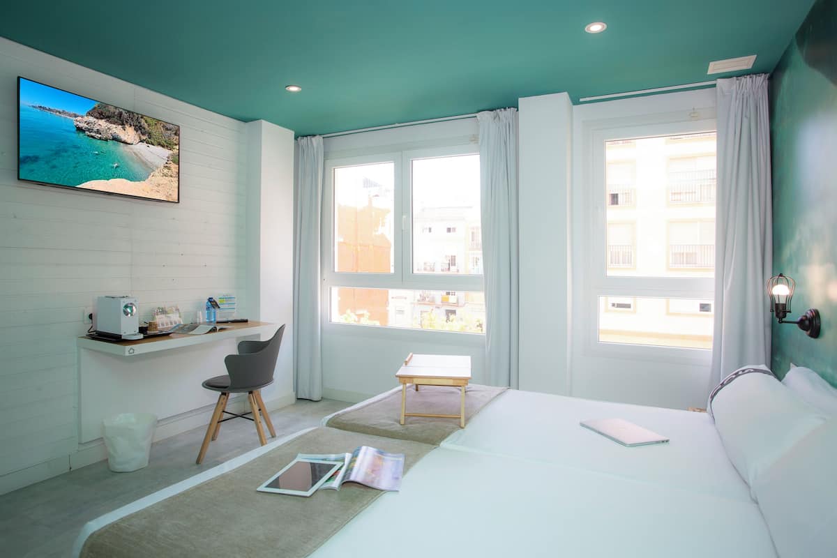 Een moderne hotelkamer met een bed, een bureau, een stoel, een televisie en grote ramen.