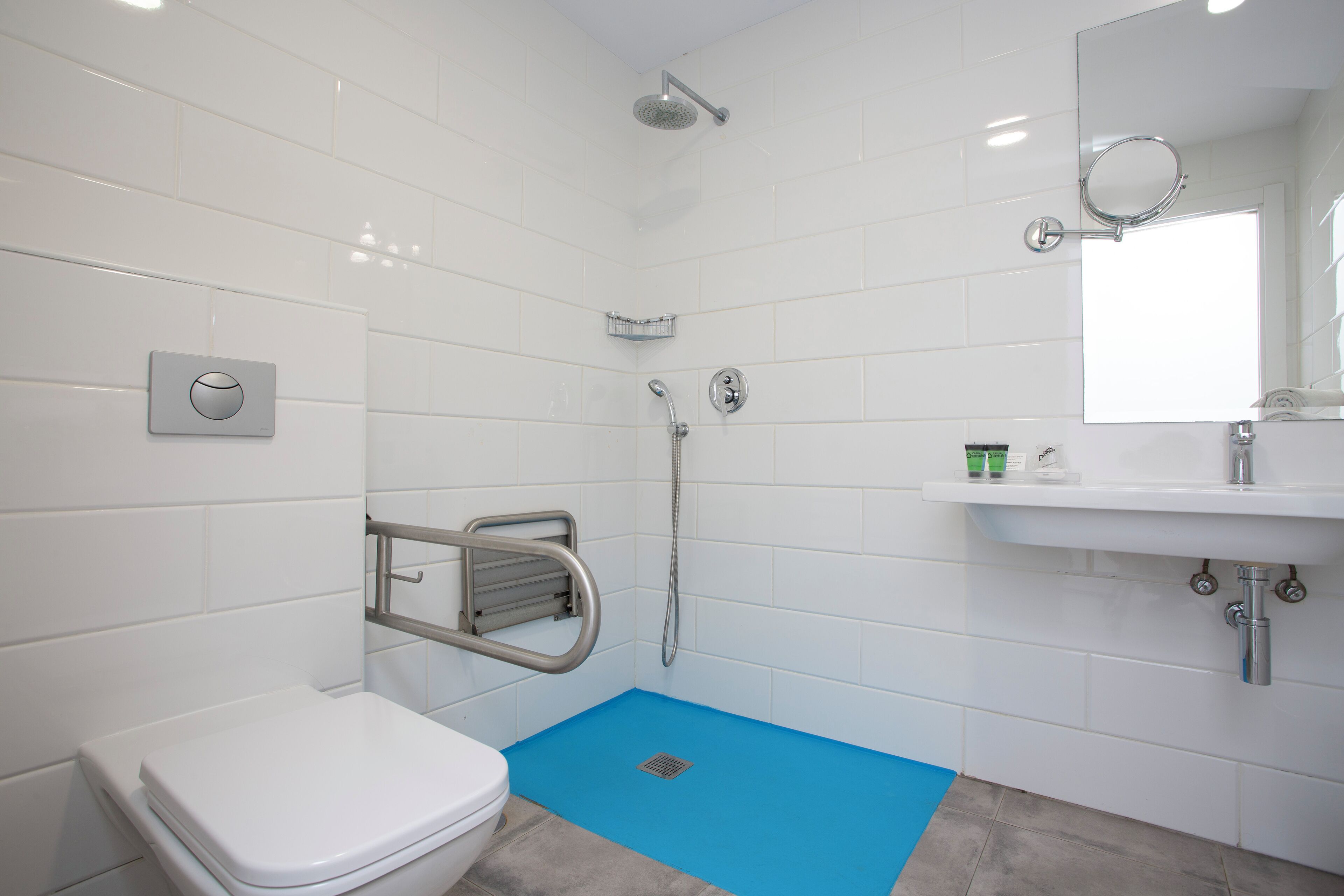 A modern bathroom with a white toilet, a shower, a sink, and a blue floor mat.