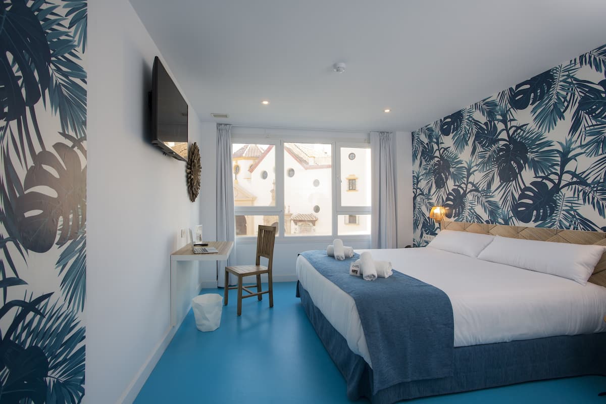 Een hotelkamer met een bed, een bureau, een stoel en uitzicht op gebouwen door het raam.