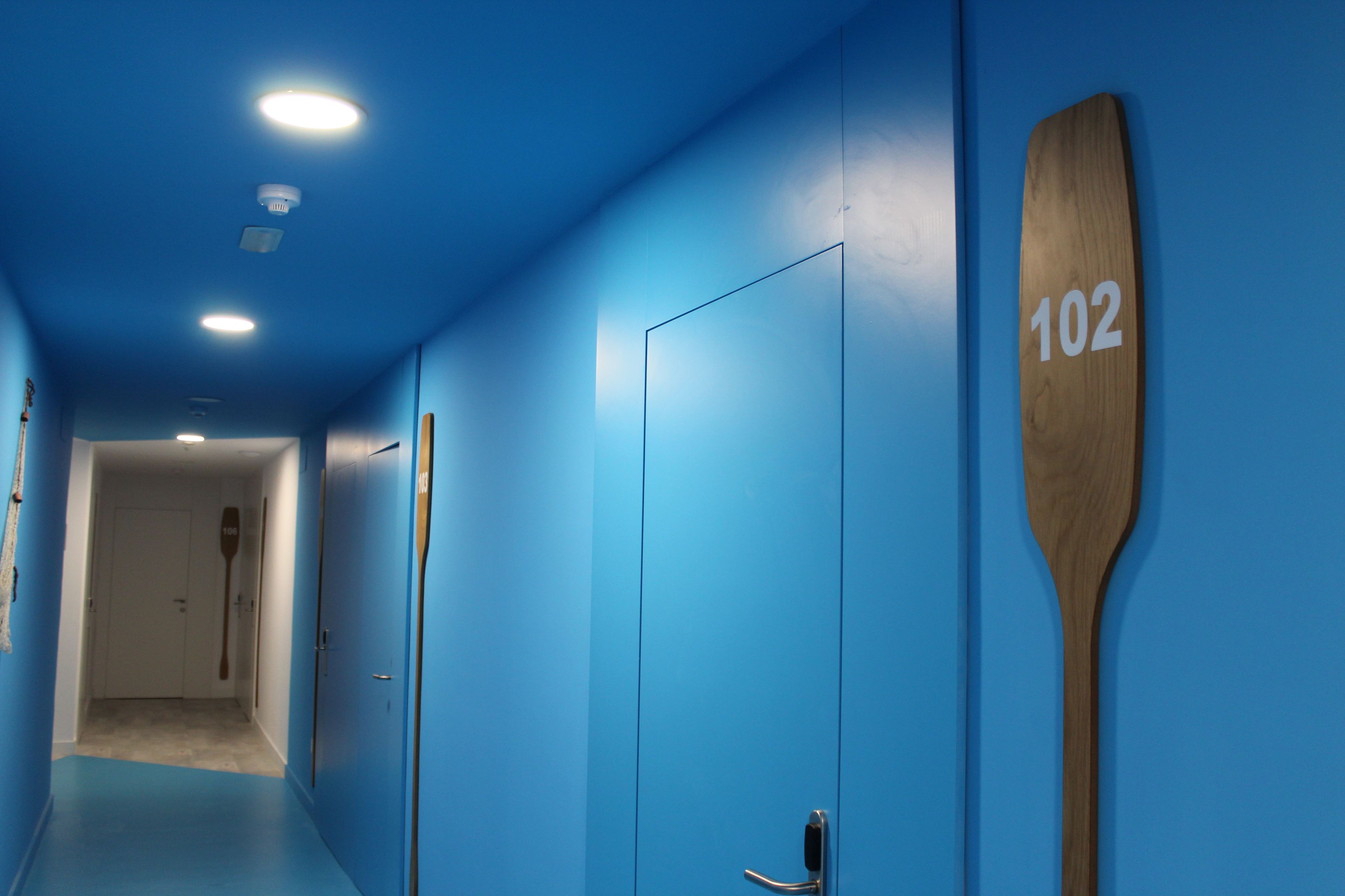 A hallway with blue walls, a wooden paddle with the number 102, and a door at the end.