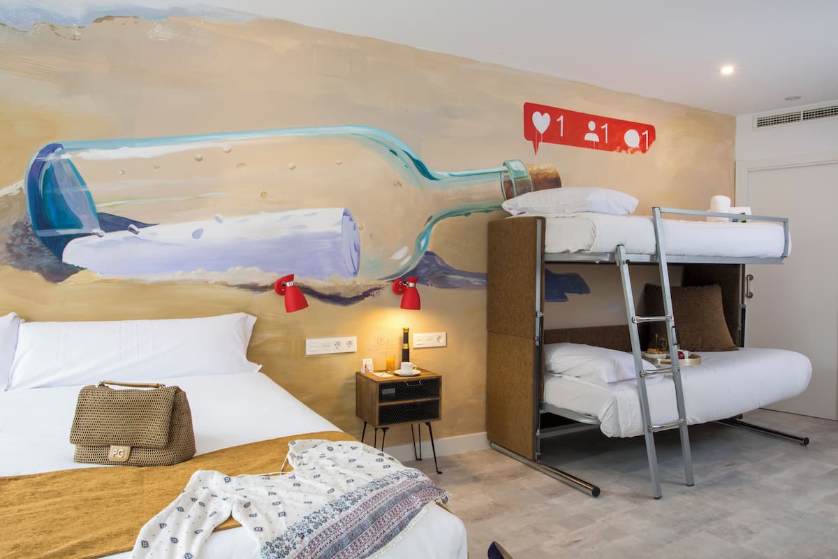Hotelkamer met een stapelbed, een enkel bed, nachtkastje met lamp, wanddecoratie van een fles en een bordje met informatie over de faciliteiten.