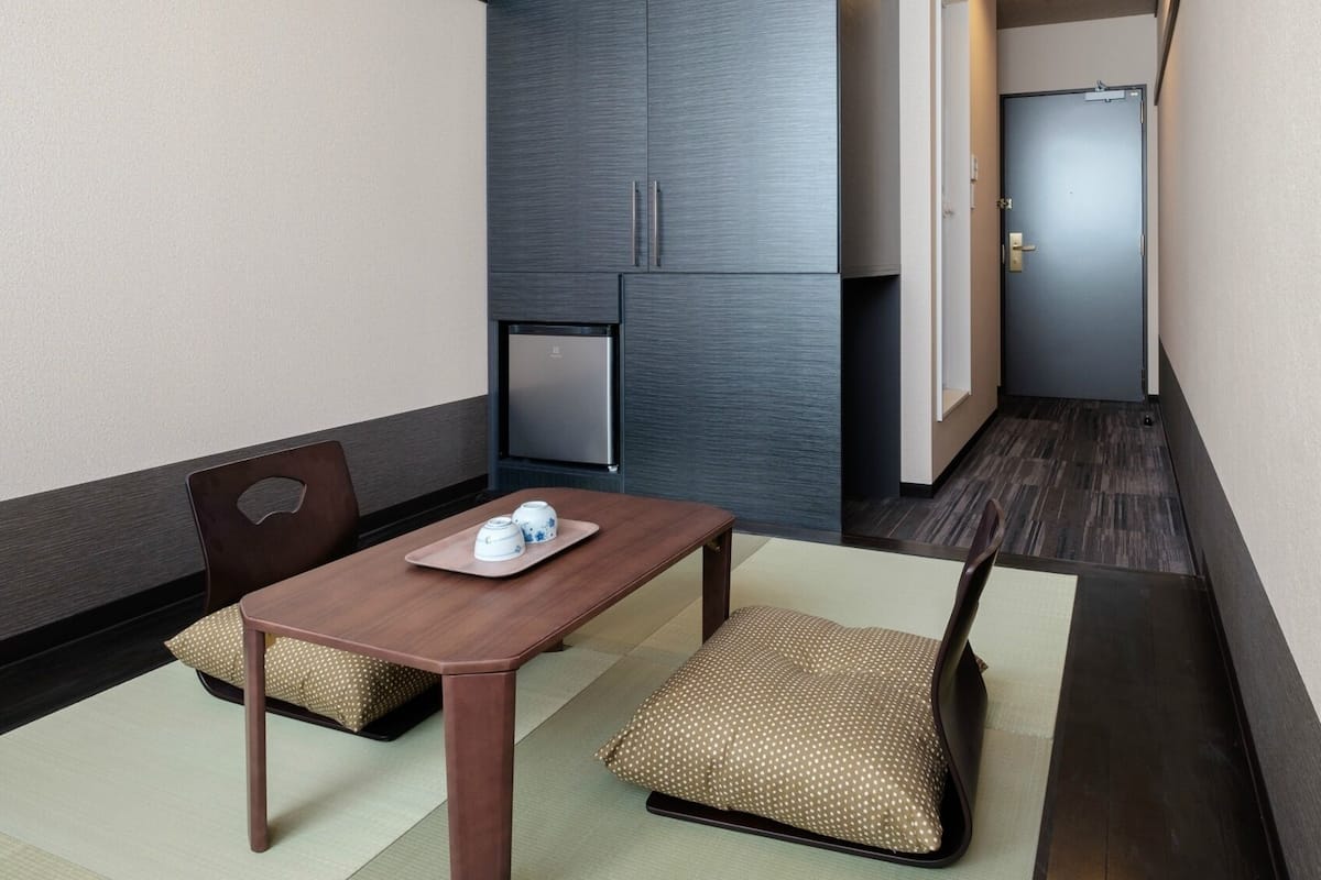 A small hotel room with a wooden table, two chairs, a refrigerator, and a door.