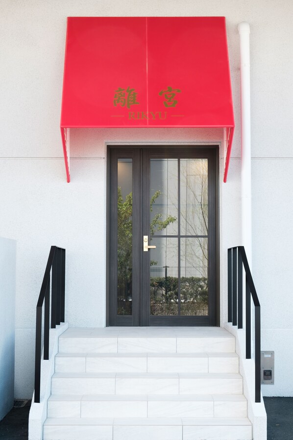 A building entrance with a red awning, a glass door, and a set of white stairs leading up to the entrance.