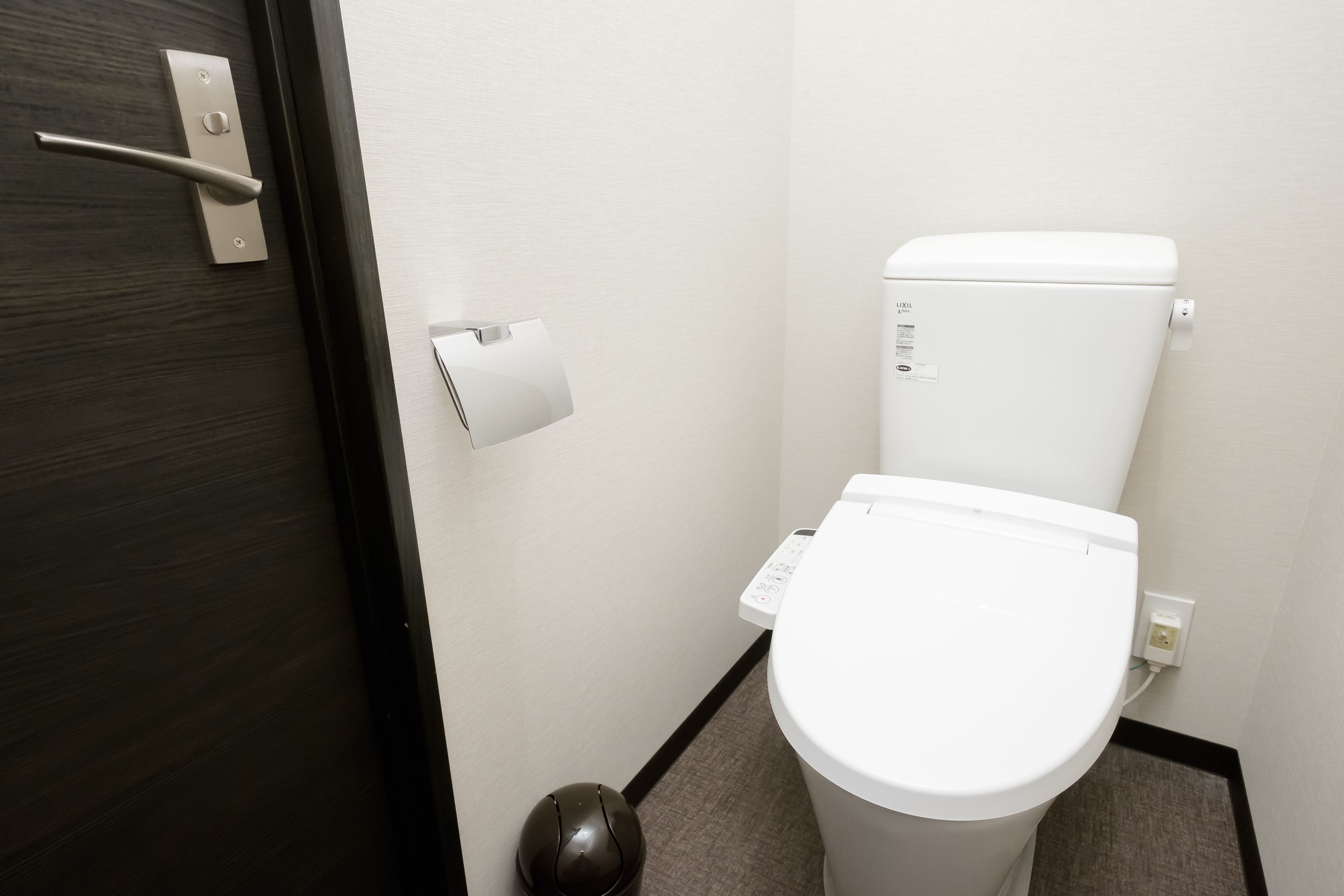 A small, modern bathroom with a white toilet, a paper towel dispenser, and a door with a handle.