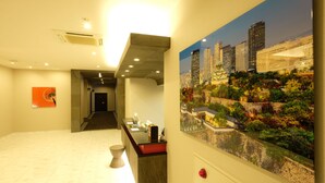 A hotel reception area with a modern design, a reception desk, a staircase, and a large cityscape painting on the wall. - The Premium Hotel in Rinku (Izumisano)