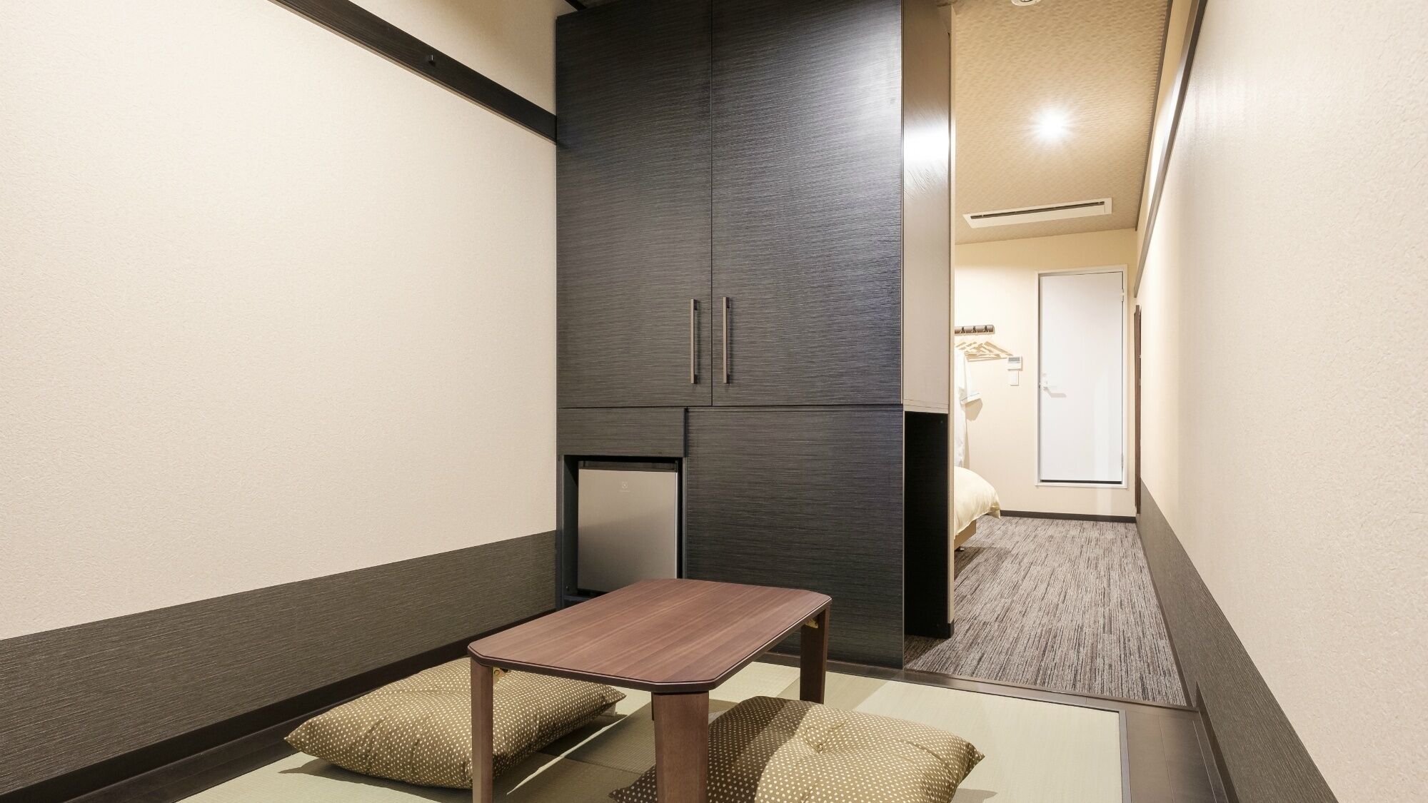A narrow hallway with a small table and cushions, a dark cabinet, and a door leading to a bedroom.