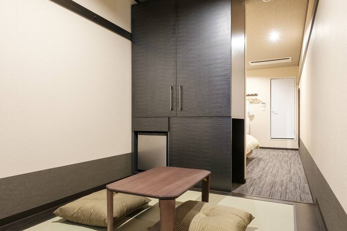 A narrow hallway with a small table and cushions, a dark cabinet, and a door leading to a bedroom.