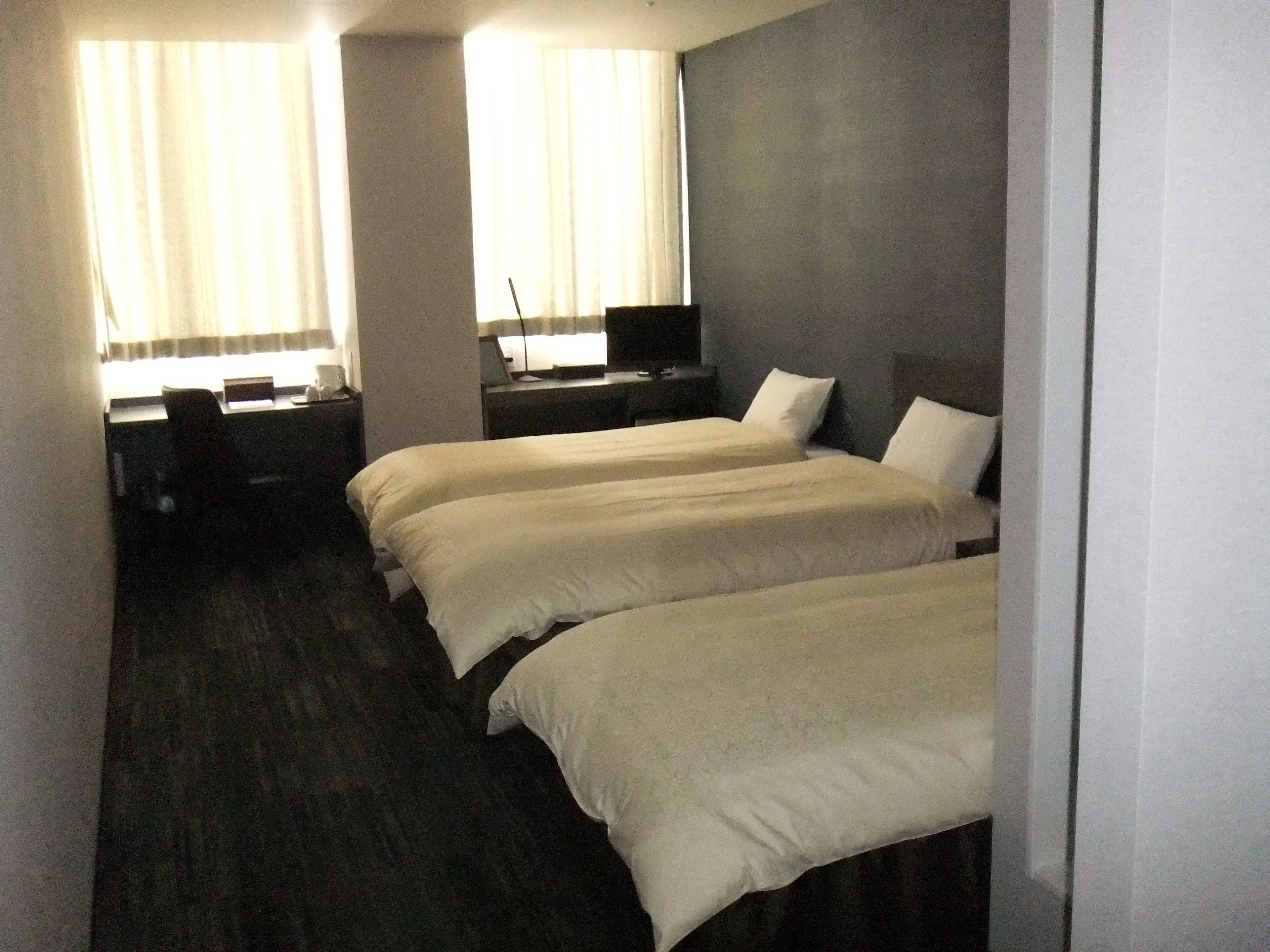 Een hotelkamer met twee eenpersoonsbedden, een bureau met stoel, een computer en een raam met gordijnen.