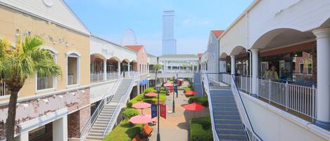A multi-level shopping mall with a central atrium, escalators, and outdoor seating areas.