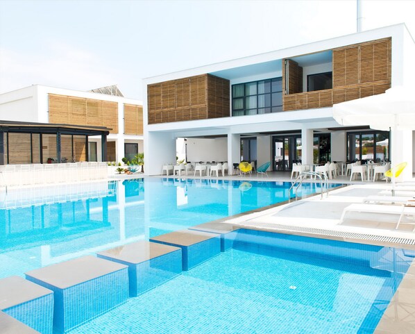 A modern hotel with a swimming pool, outdoor seating, and a covered patio area. - The OAK Hotel Keramoti (Nestos)