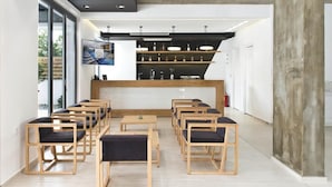 Un intérieur moderne avec des chaises et des tables en bois disposées en demi-cercle, un comptoir d’accueil avec des étagères remplies de bouteilles et une grande fenêtre laissant entrer la lumière naturelle.