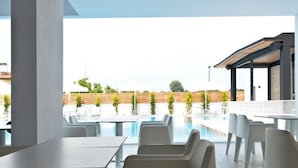 Un espace extérieur moderne, aménagé avec des sièges, une piscine, des chaises blanches et un coin salon abrité.