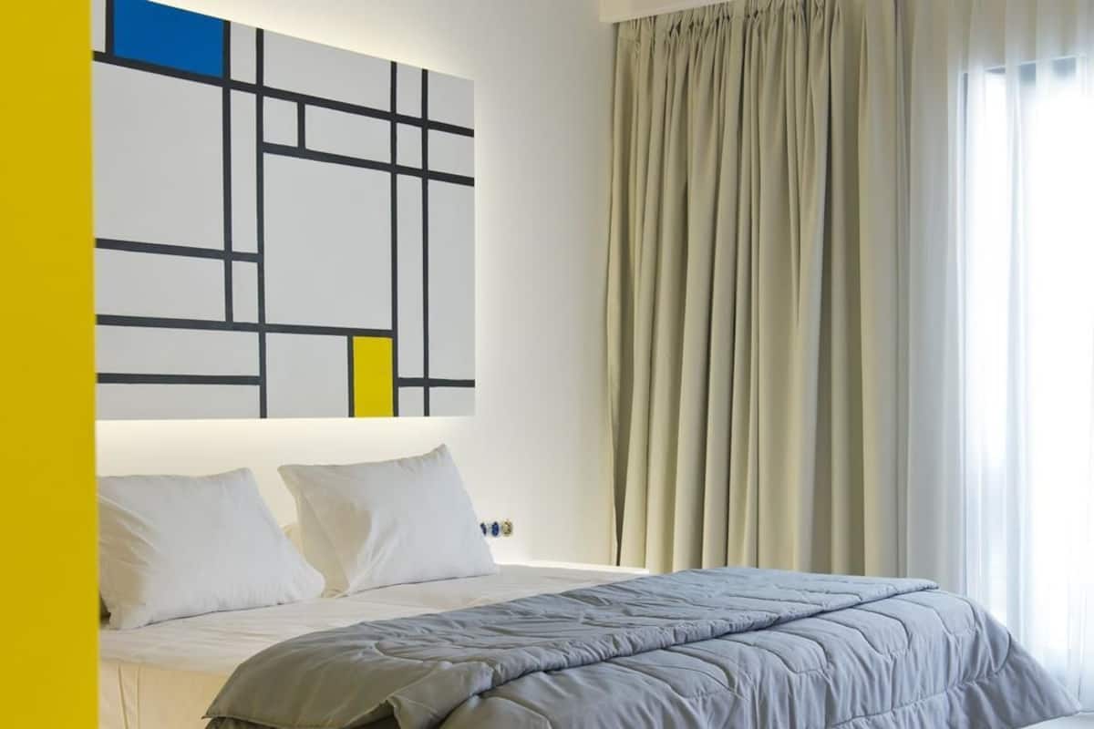 Un dormitorio moderno con una cama, almohadas blancas, un edredón gris y una obra de arte geométrica en la pared.