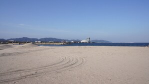 A sandy beach with a clear sky, a few buildings in the distance, and mountains in the background. - HOTEL AreaOne SAKAIMINATO MARINA (Sakaiminato)