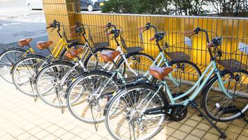 A row of bicycles parked against a yellow wall with a metal fence.